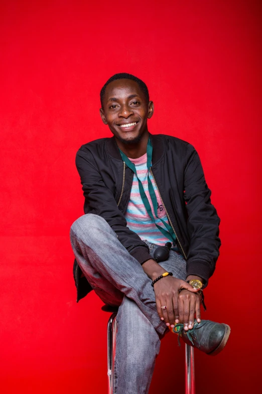 a smiling young man posing with a red wall in the background