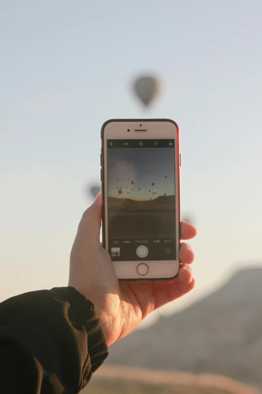 someone is holding their cell phone while  air balloons fly