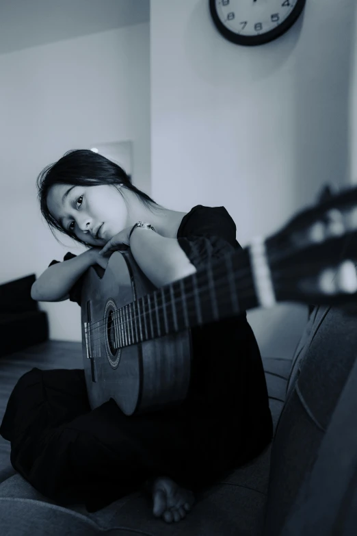 a person sitting with their guitar, holding their hand up to their neck