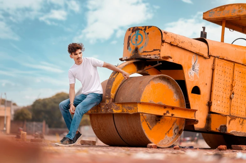 the man is posing next to an old yellow construction vehicle