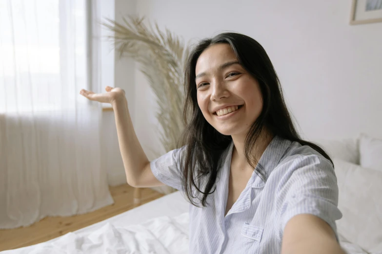 woman smiling in bedroom by window with hand up