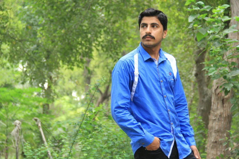 man in blue shirt standing by trees looking ahead