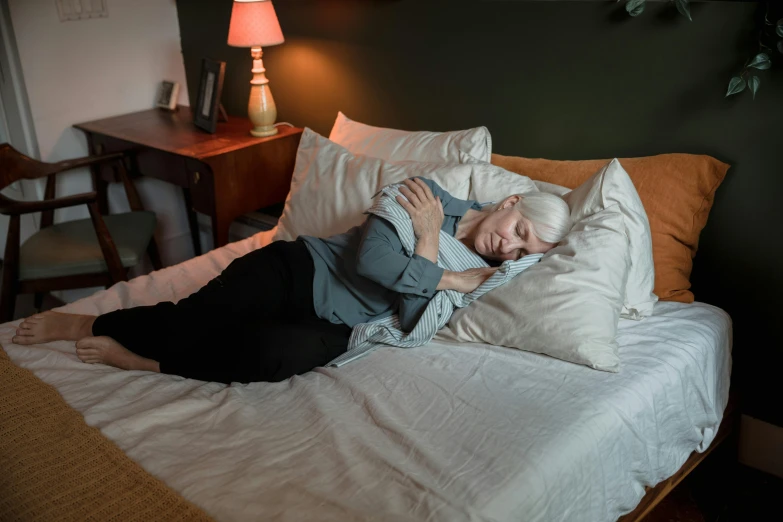 an older woman is laying on her side while holding her head in pillows