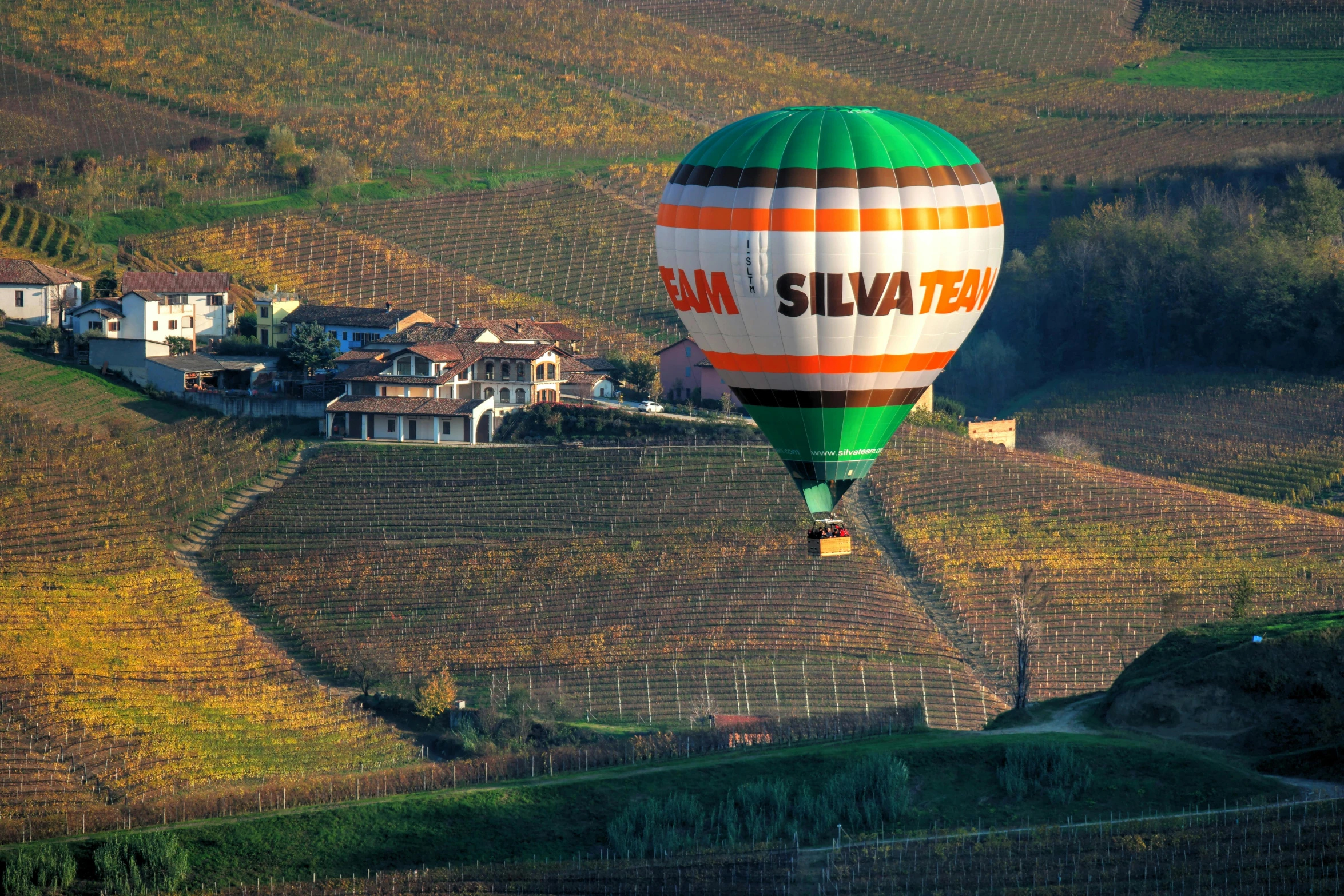 the large green  air balloon is flying over the rural countryside