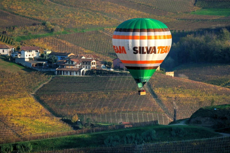 the large green  air balloon is flying over the rural countryside
