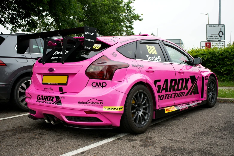 a car painted pink sits in a parking lot next to a parked truck