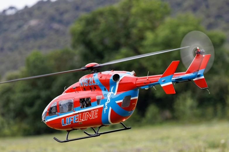 a red and blue helicopter is landing on some grass