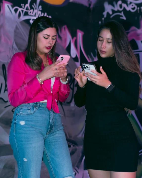 two women in front of graffiti and looking at their cell phones