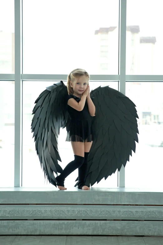 a little girl dressed in black has a large black wings on her body