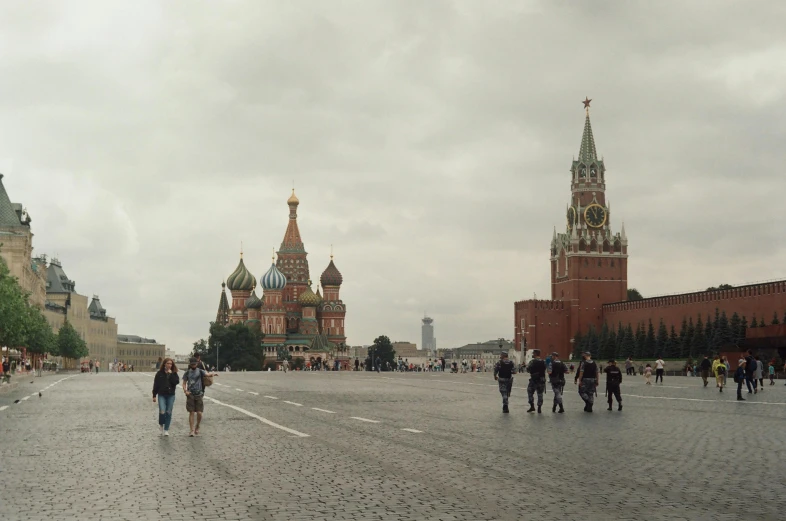 people walk down a stone street lined with tall red buildings