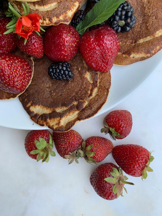 two stacks of pancakes on a white plate next to some berries