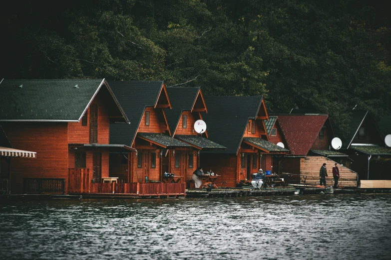 a row of red cabins on water with houses in the background