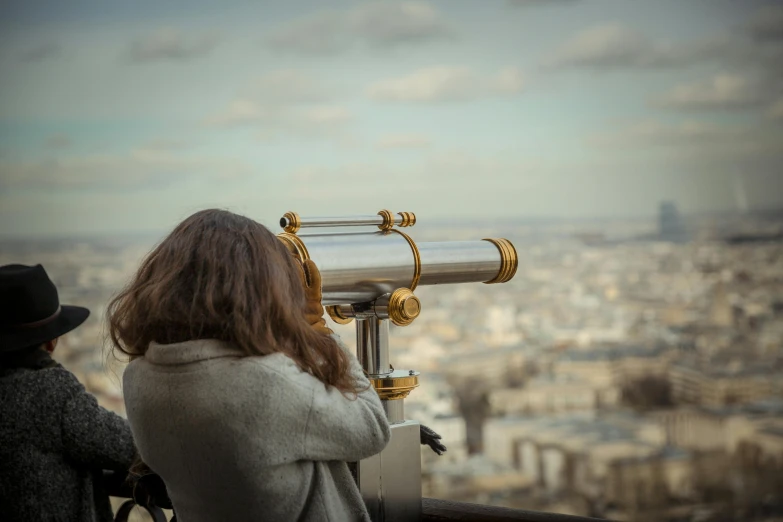 two people looking over a city from top of the building with a telescope