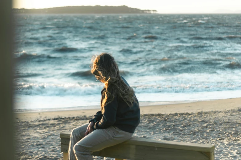 woman sitting on bench next to beach with ocean and mountain in background