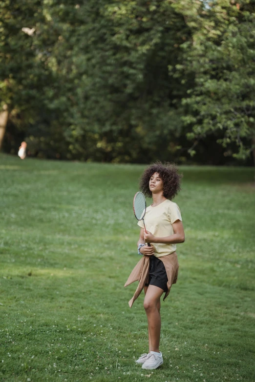 a woman with an afro in a park holding onto a racket