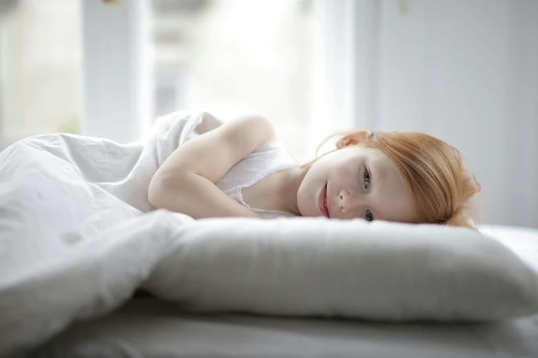 a beautiful woman laying on top of a bed under a white blanket