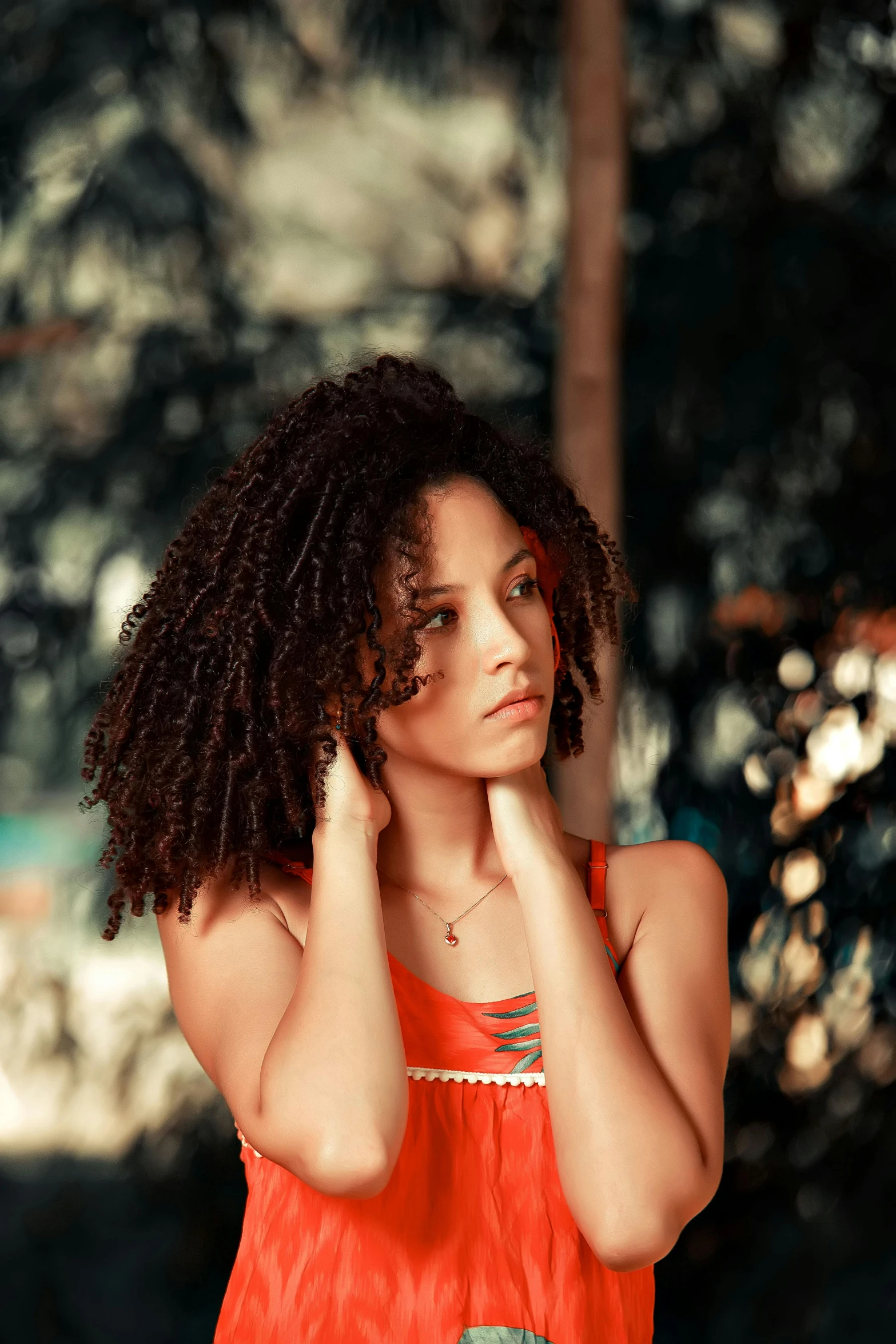 the young woman poses near a wooded area with her hand to her head