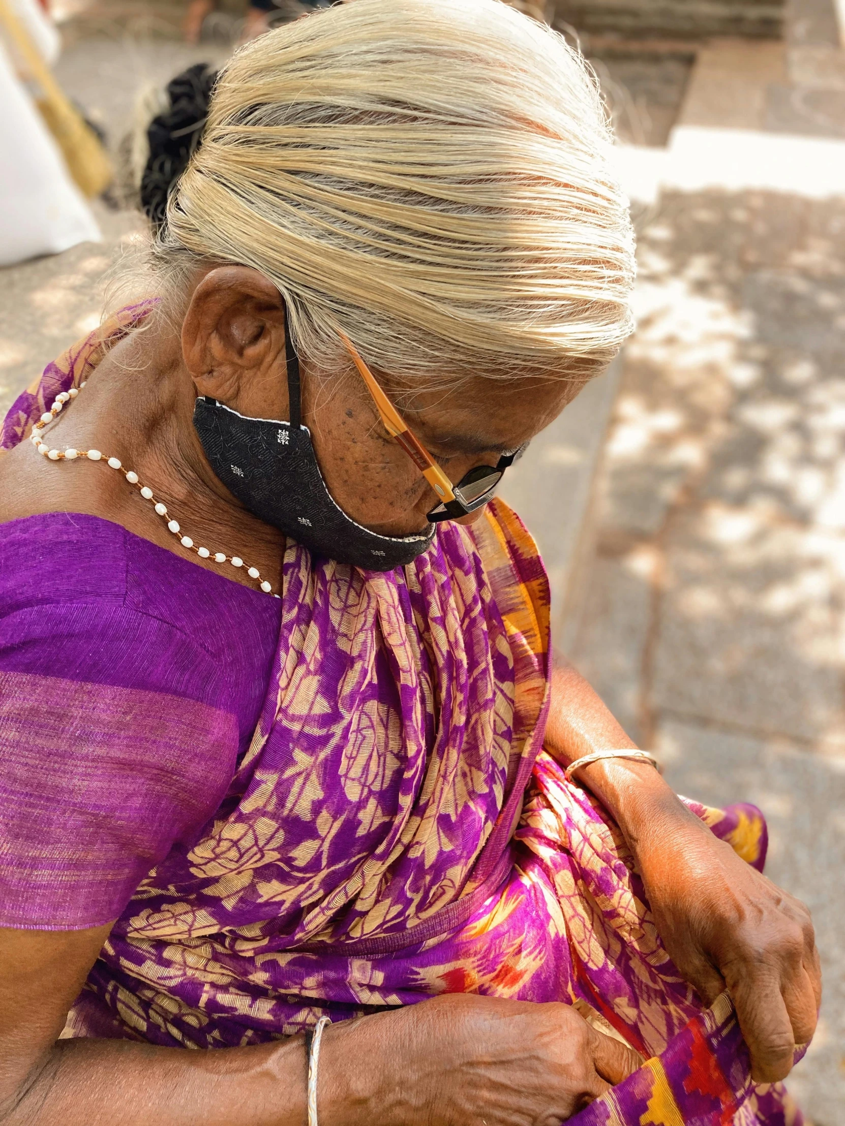 a woman in a yellow and pink dress looks down as she holds onto a cellphone