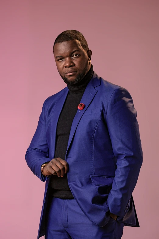 man in blue jacket posing for camera in front of a pink wall