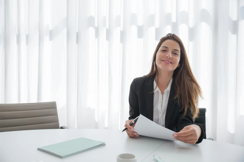 woman in a suit sitting at a table with papers and a pen