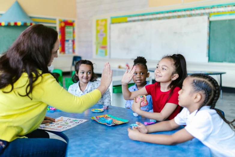 a group of children sitting around a table while an adult interacts with them