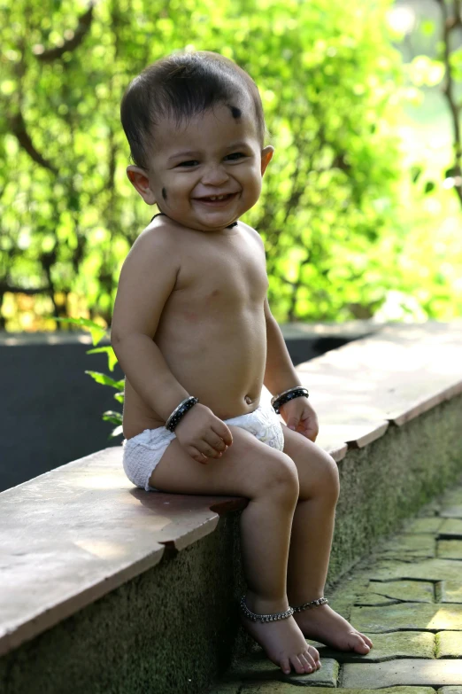 a toddler smiles while sitting on brick ledge