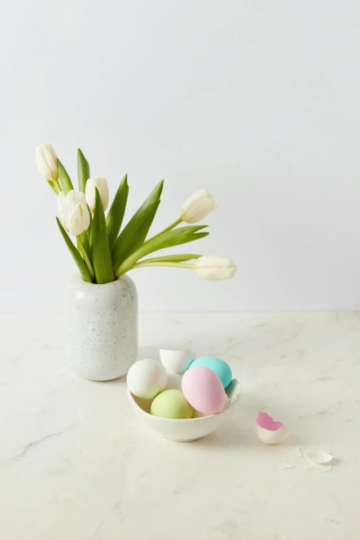 a vase with flowers and eggs near it on a counter