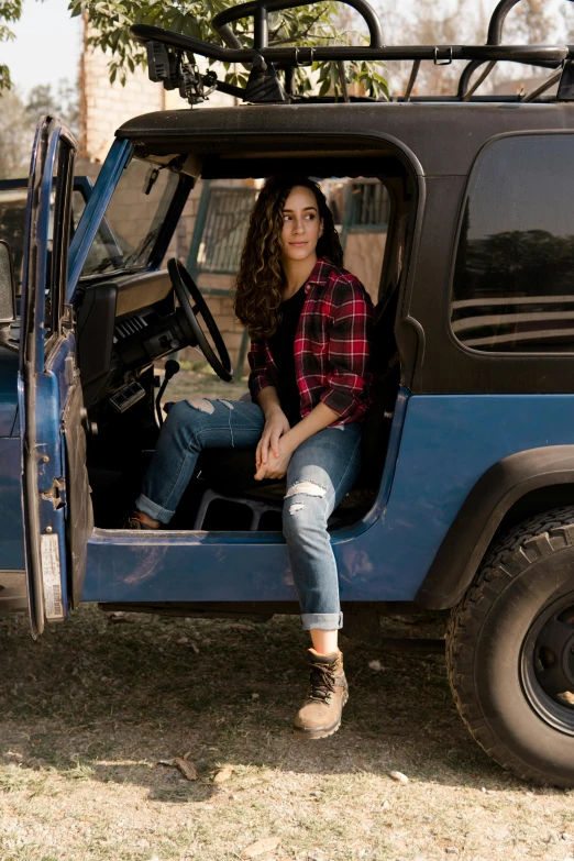 a young lady sitting inside of a parked blue jeep