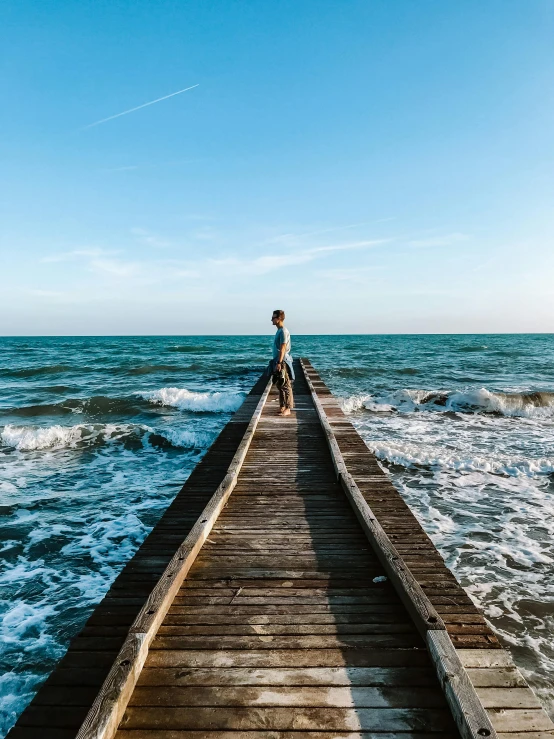 person standing on a long pier looking out at the ocean