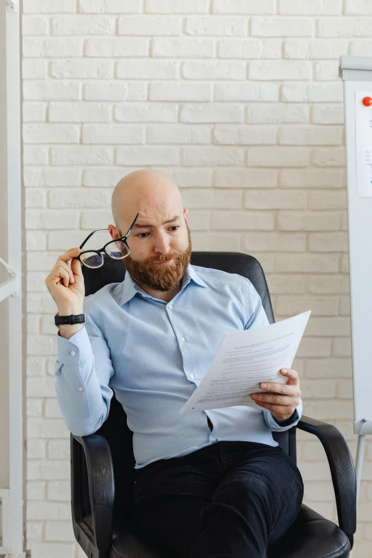 a man in blue shirt sitting on chair reading a document