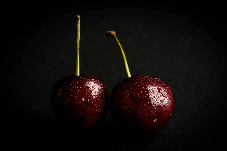 two cherries in the dark with water droplets on them