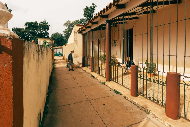 a side walk has a fence on the wall and two men in the doorway