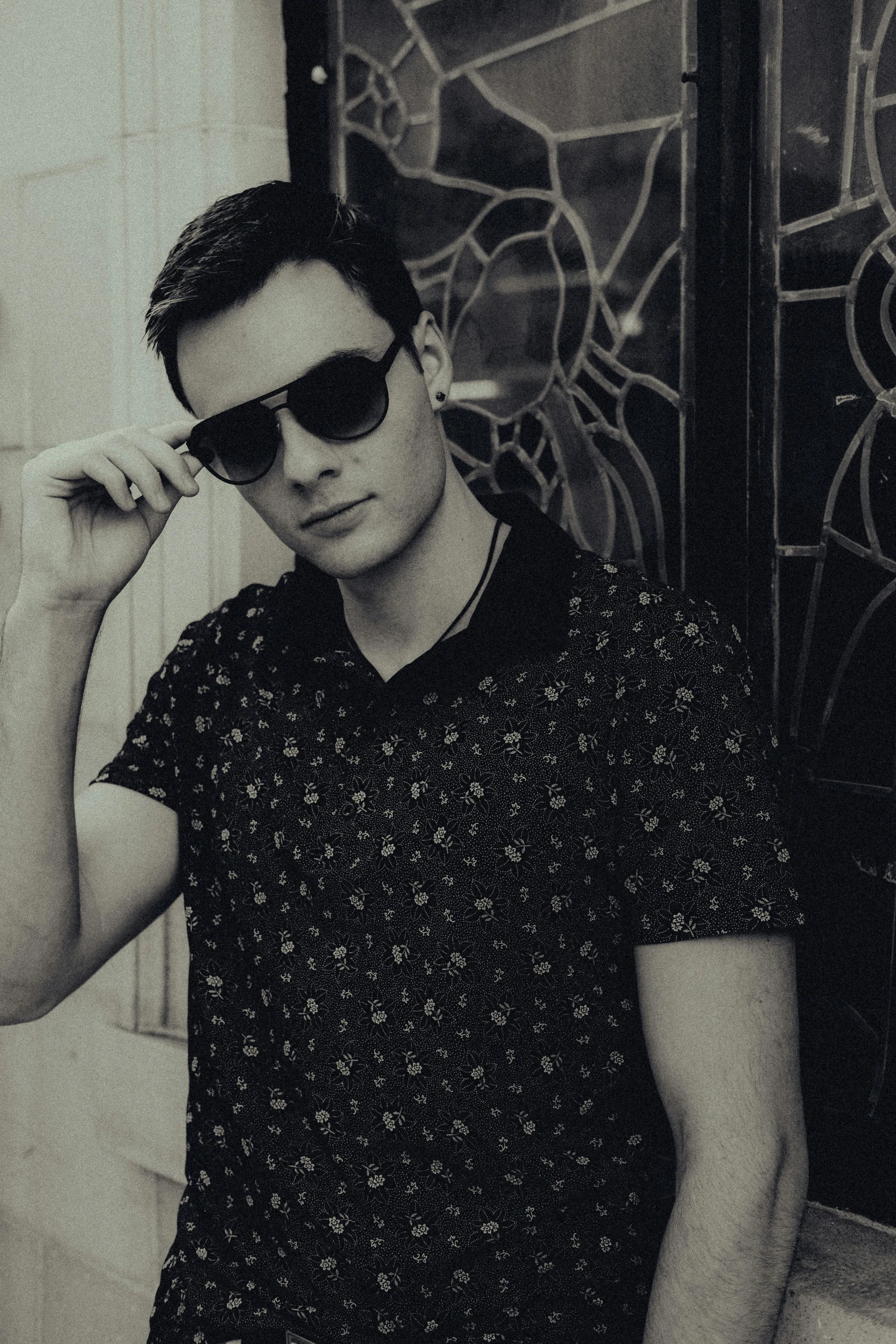 a young man in sunglasses is standing near a wall