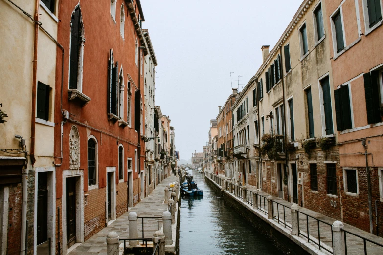 small boats are coming down the water beside buildings