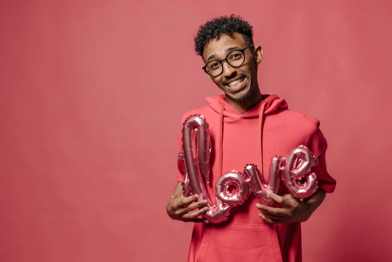 man standing and posing with letters spelling love on pink