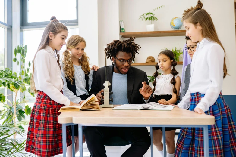 a teacher sitting at a table with several children looking at an book