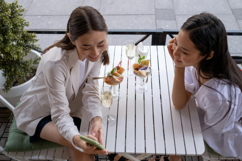 two women sitting at an outdoor table with drinks on them