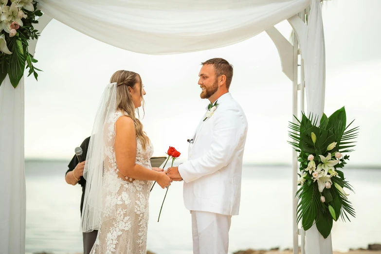 a married couple on their wedding day, under a white chute, with a single rose in the middle