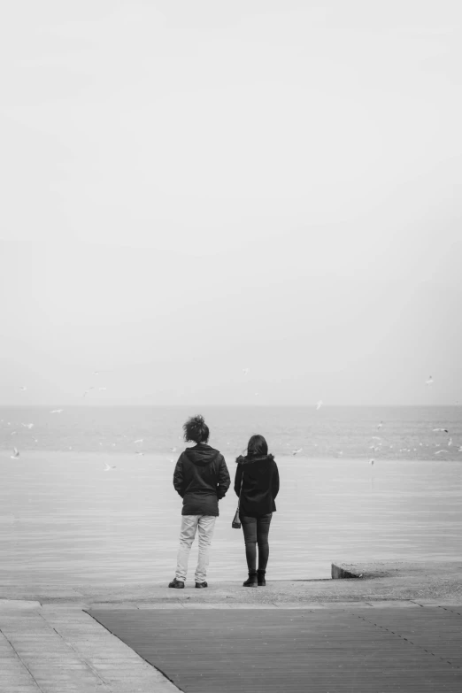 two people standing on a dock staring at an ocean