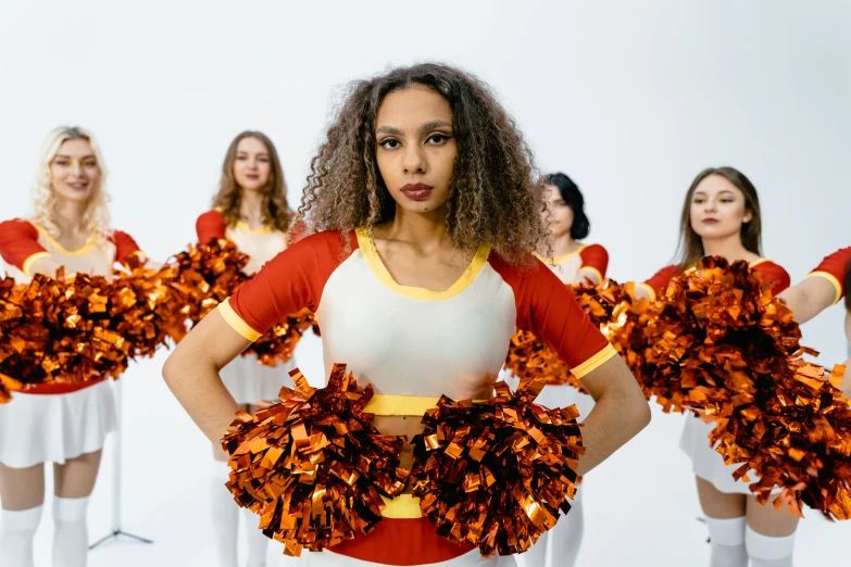 a woman standing in front of three other women holding orange and white cheerleaders