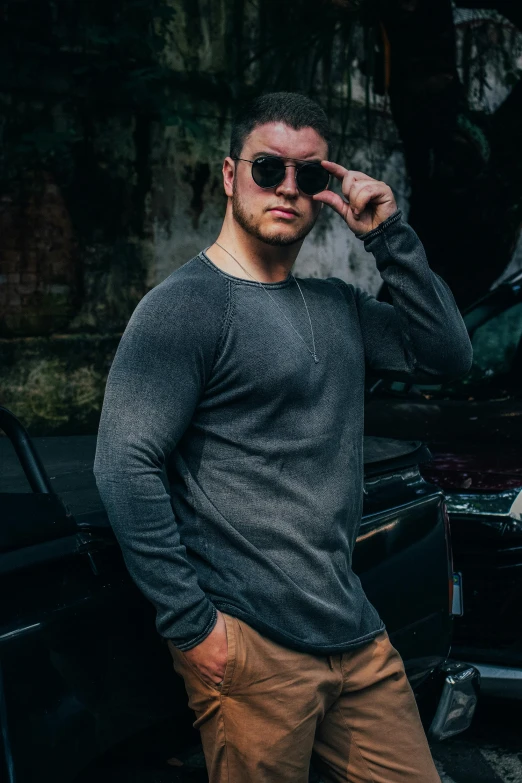 a man standing outside next to a car while wearing sunglasses