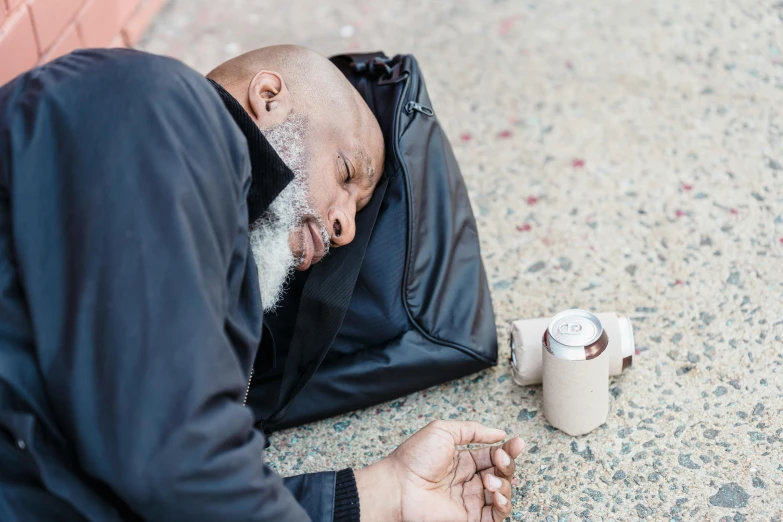 an old man laying on the ground with a coffee cup and jacket on