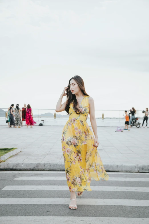 a woman in a yellow floral dress talking on her phone while walking across a street