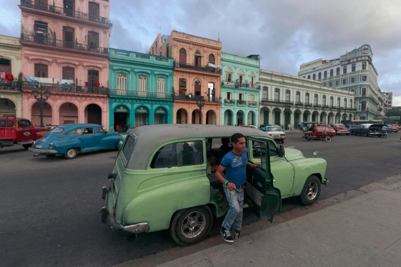 two men standing next to an old green car