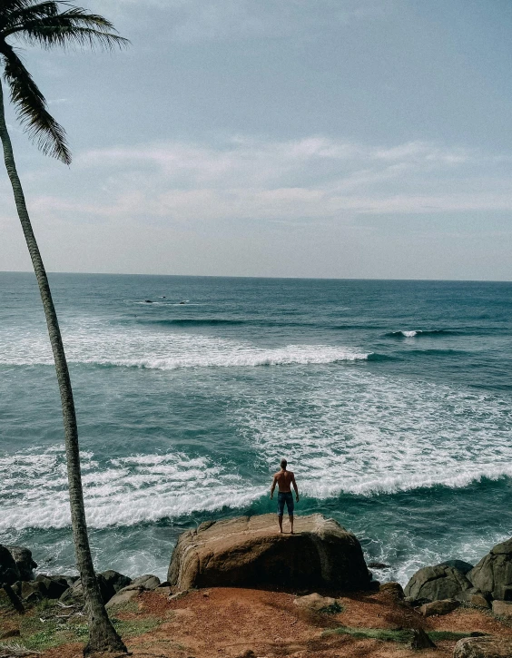 a lone man standing on the rocks looking out at the ocean