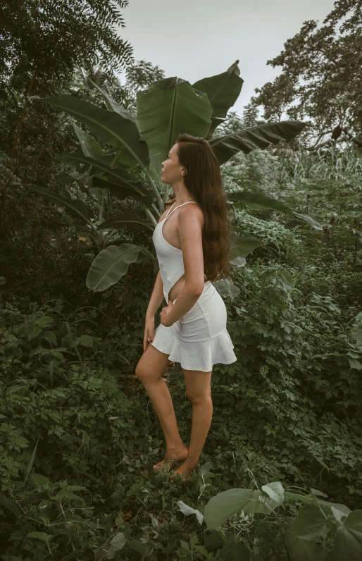 a woman in white stands alone near a large green plant