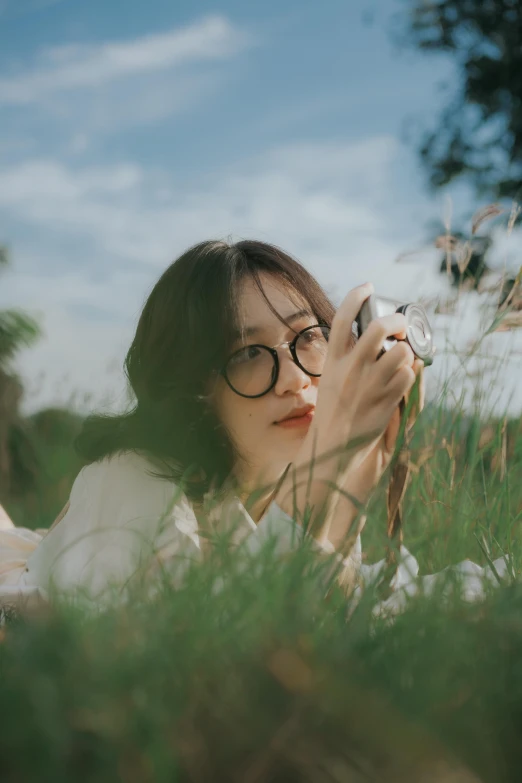 a woman in glasses sitting in the grass holding a cell phone