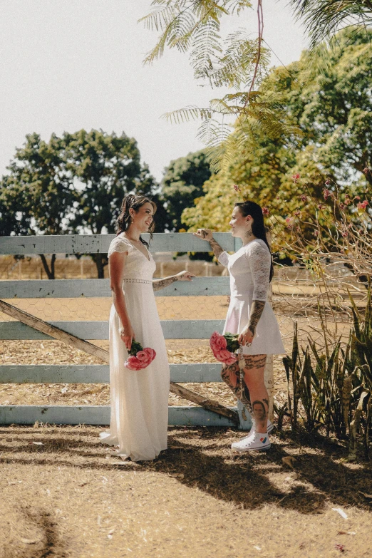 two women standing together near a white fence