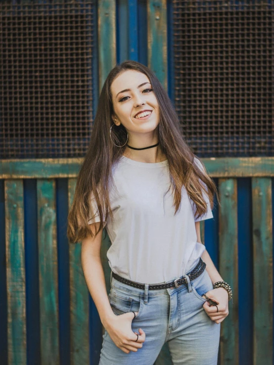 woman in jeans smiling for a picture by an old fence