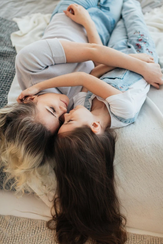 two girls lie down and laugh next to each other on the bed